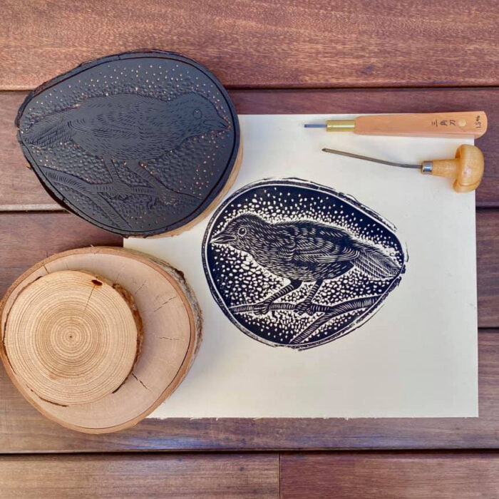 Woodblock plate, carving tools and print of woodblock on wood table.